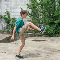 a boy in a teal shirt and shoes kicks a hacky sack