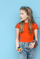 a girl in a red shirt, sunglasses, and scrunchies on her arm holds a hacky sack